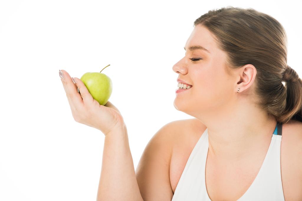 молода усміхнена жінка з надмірною вагою дивиться на зелене яблуко ізольоване на білому
 - Фото, зображення