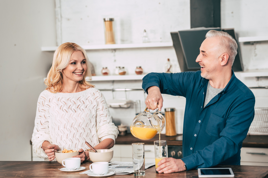 cheerful man pouring orange juice in glass near attractive wife  - Photo, Image