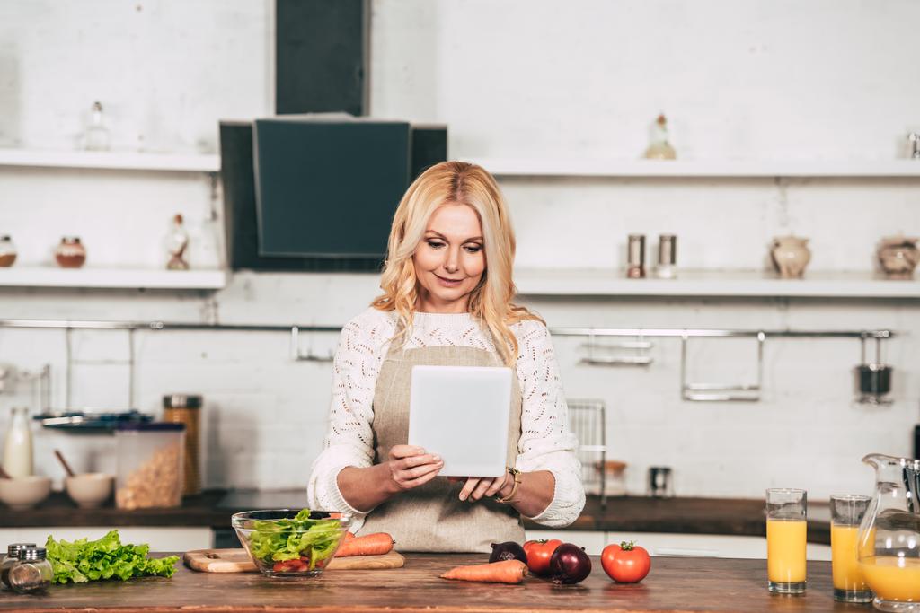donna felice utilizzando tablet digitale mentre in piedi in cucina vicino alle verdure
 - Foto, immagini