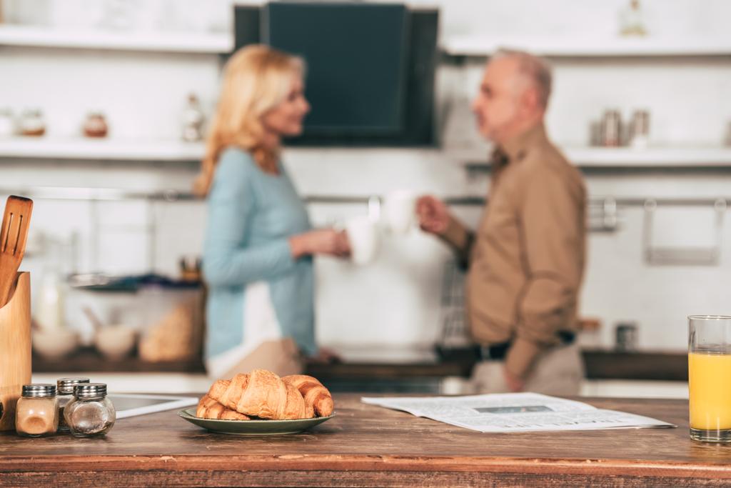 selective focus of tasty croissants on plate near glass of orange juice with couple on background - Photo, Image
