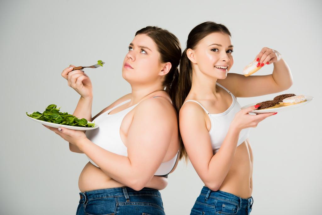 glückliche schlanke Frau isst Donuts, während traurige übergewichtige Frau grüne Spinatblätter isst - Foto, Bild