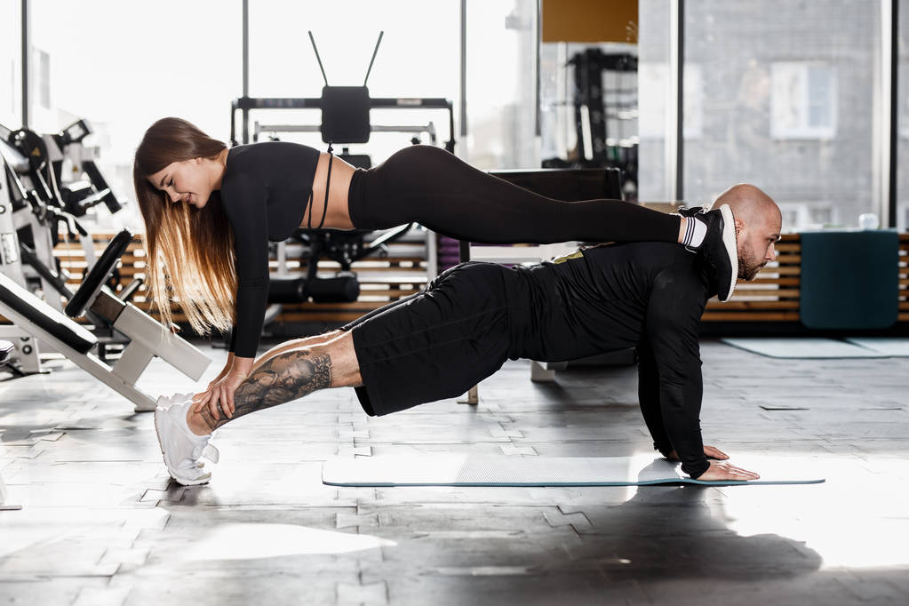 Atletische paar moeilijke sport doet oefenen waar het meisje staat in de plank op een man die in de plank in de moderne sportschool staat - Foto, afbeelding