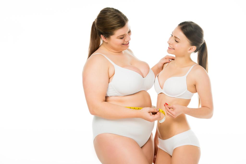 щасливе тіло позитивна жінка з надмірною вагою дивиться на струнку жінку, тримаючи вимірювальну стрічку разом ізольовано на білому
 - Фото, зображення