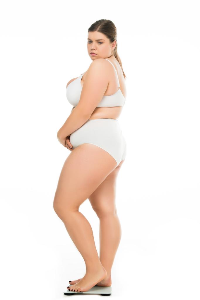 vista lateral de triste joven mujer con sobrepeso en ropa interior de pie en escamas aisladas en blanco, perder peso concepto
 - Foto, imagen