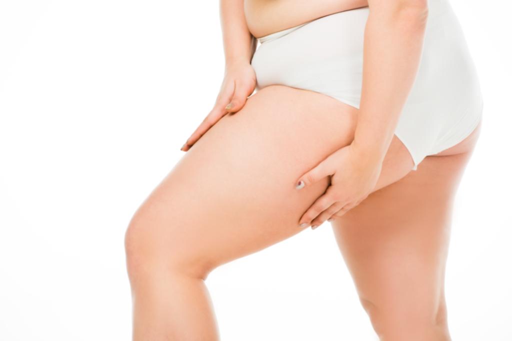 visão cortada de mulher com sobrepeso posando com as mãos sobre a perna isolada em branco, conceito de positividade corporal
 - Foto, Imagem