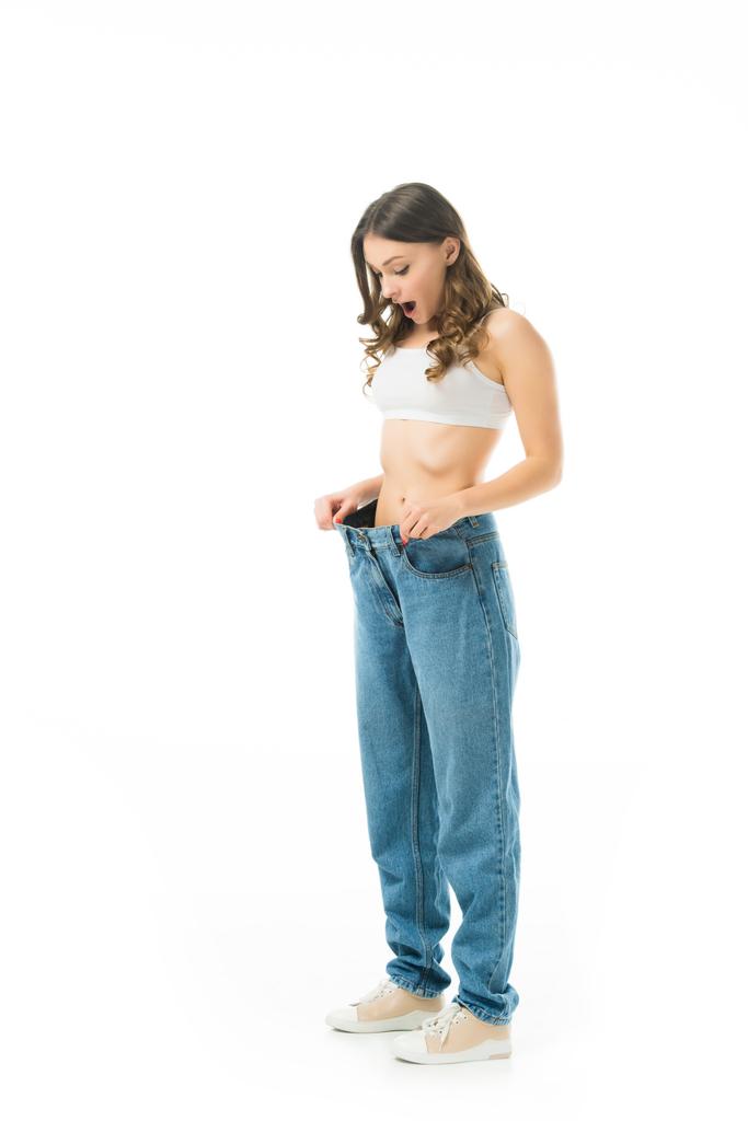 surprise mince fille regardant gros jeans isolés sur blanc, perdre du poids concept
 - Photo, image