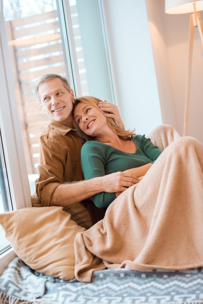 couple souriant étreignant assis sur le sol par une grande fenêtre à la nouvelle maison
 - Photo, image