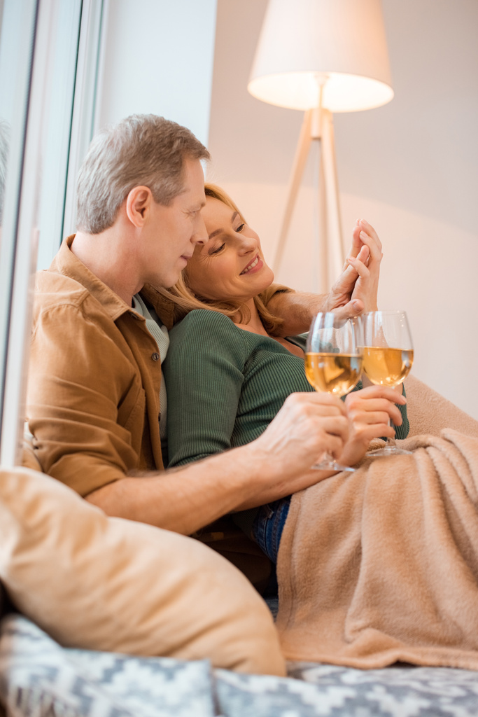 happy couple holding glasses of white wine while resting under soft fleece blanket - Photo, Image