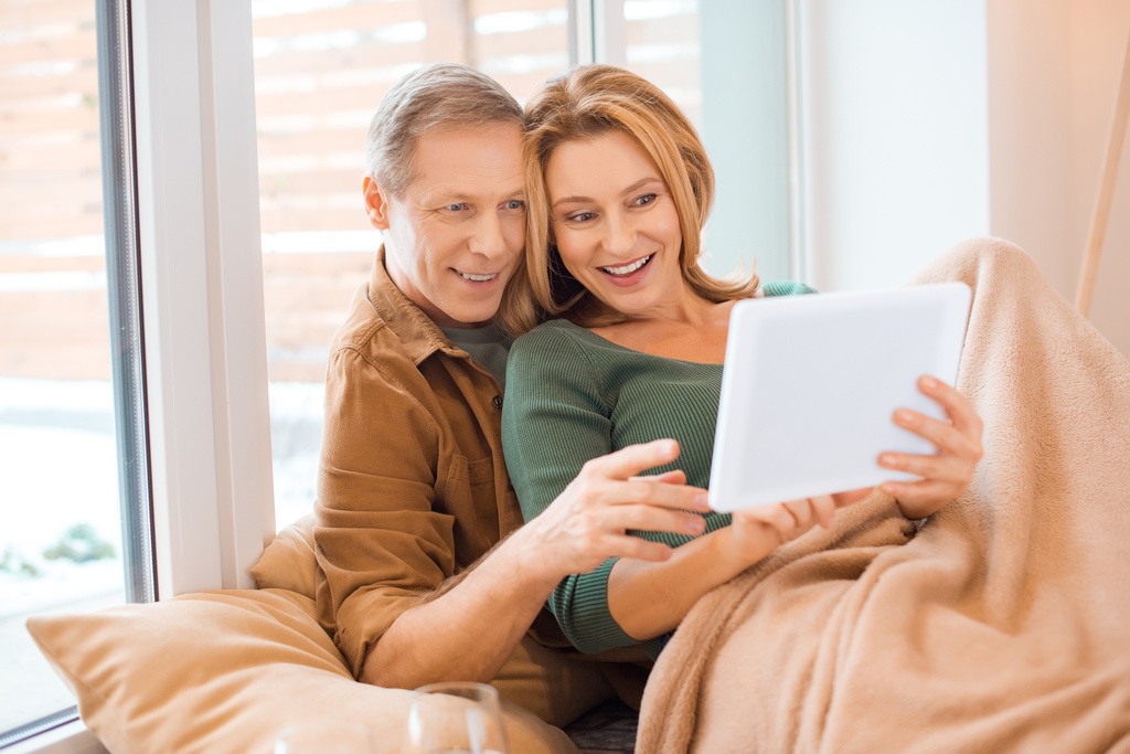 smiling couple using digital tablet together while sitting by window - Photo, Image