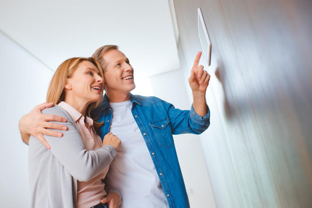 Lächelnder Mann zeigt auf Smart Home Bedienfeld, während er Ehefrau umarmt - Foto, Bild