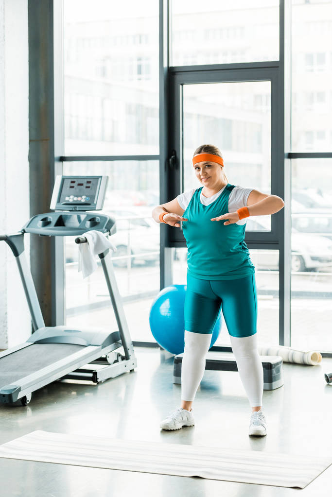 overgewicht vrouw uitrekken terwijl je in sportkleding in de buurt van fitness mat - Foto, afbeelding