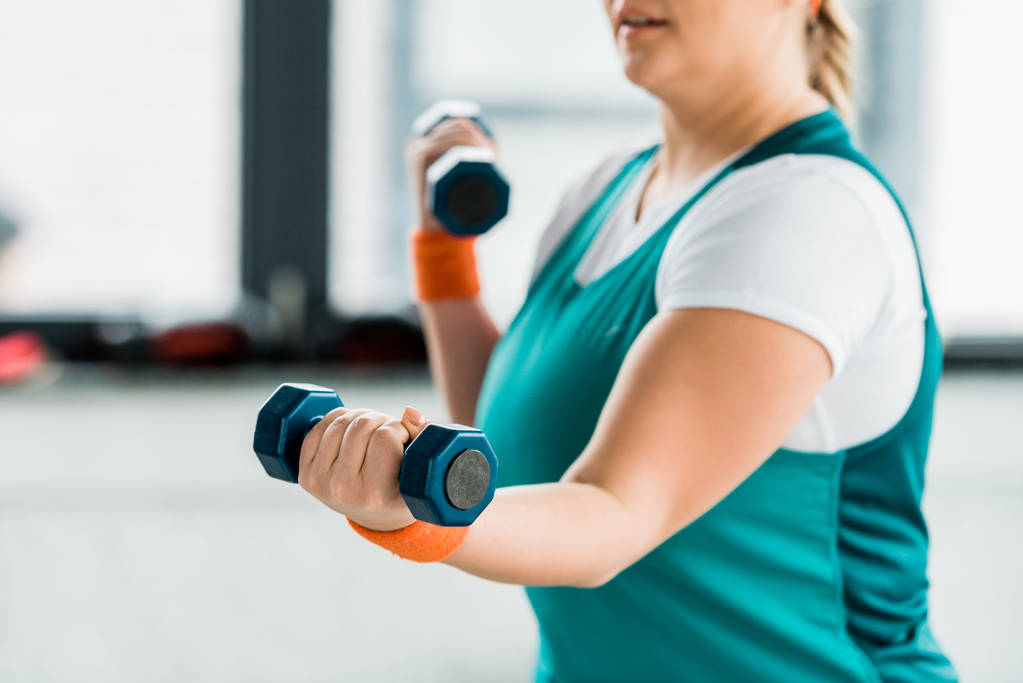 enfoque selectivo de la mujer con sobrepeso haciendo ejercicio en ropa deportiva con mancuernas
 - Foto, Imagen