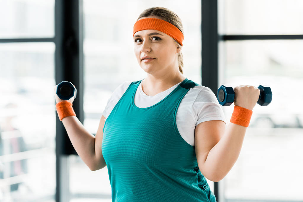 attractive plus size woman exercising with dumbbells in gym - Photo, Image