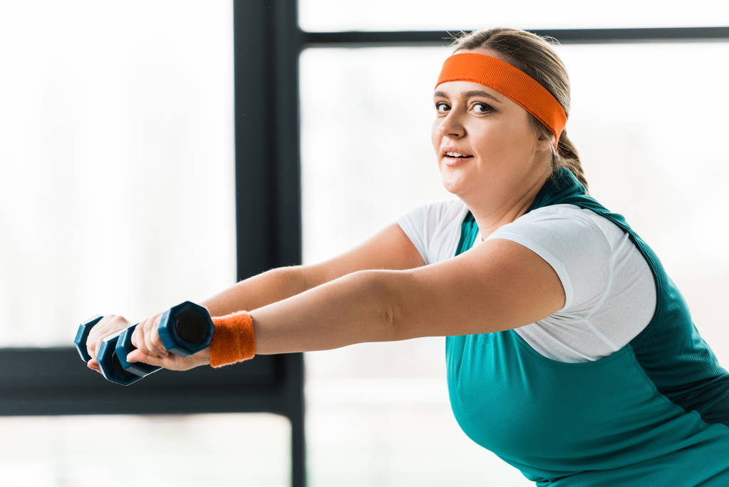 beautiful plus size woman training with dumbbells in gym - Photo, Image