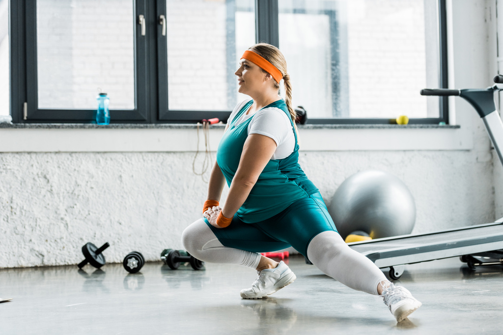smiling plus size girl in sportswear stretching in gym - Photo, Image