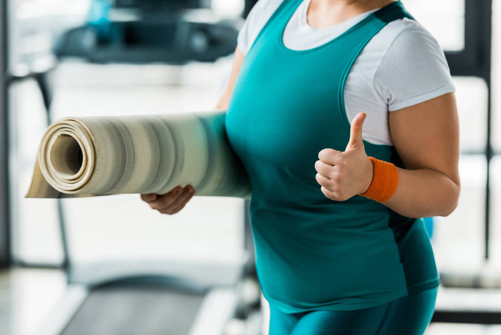 túlsúlyos nő felbukkan hüvelykujj edzőteremben fitness szőnyeg tartva vágott megtekintése - Fotó, kép