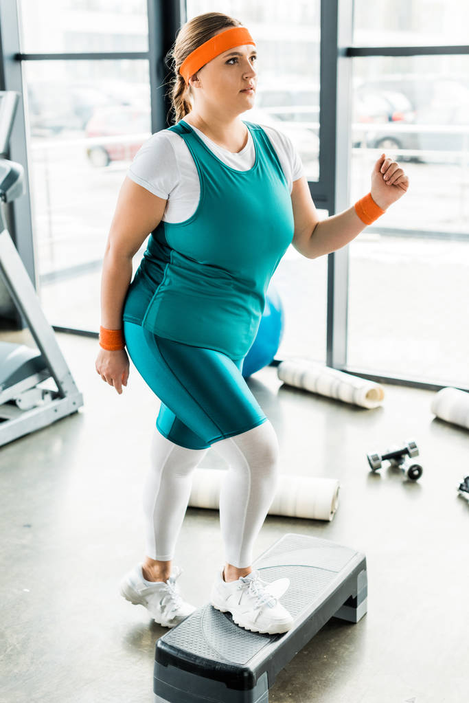Plus mat rozmiar dziewczyna ćwiczeń na platformie krok w pobliżu fitness w siłowni - Zdjęcie, obraz
