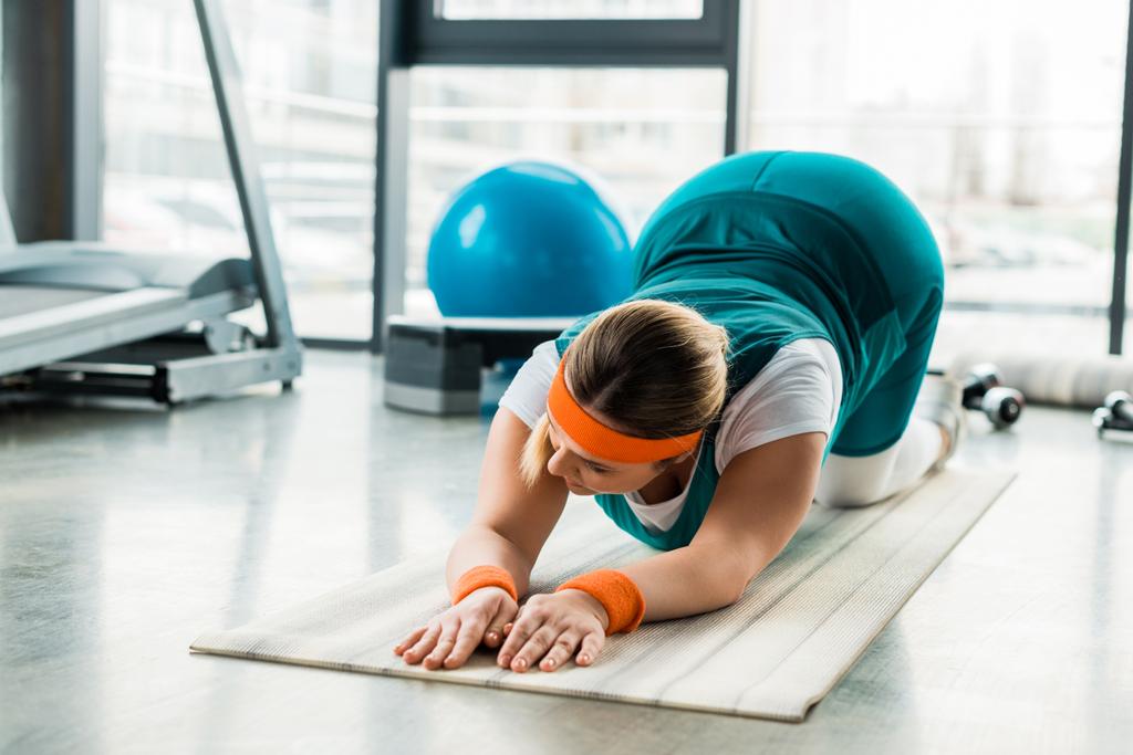 Plus-Size-Frau trainiert auf Fitnessmatte in der Nähe von Sportgeräten - Foto, Bild