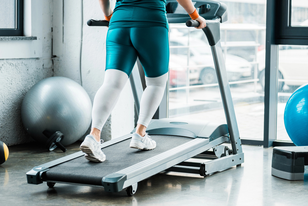 cropped view of overweight girl running on treadmill in gym - Photo, Image