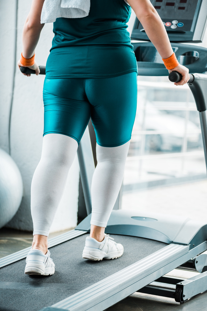 обрезанный вид плюс размер женщины упражнения на беговой дорожке в тренажерном зале
 - Фото, изображение