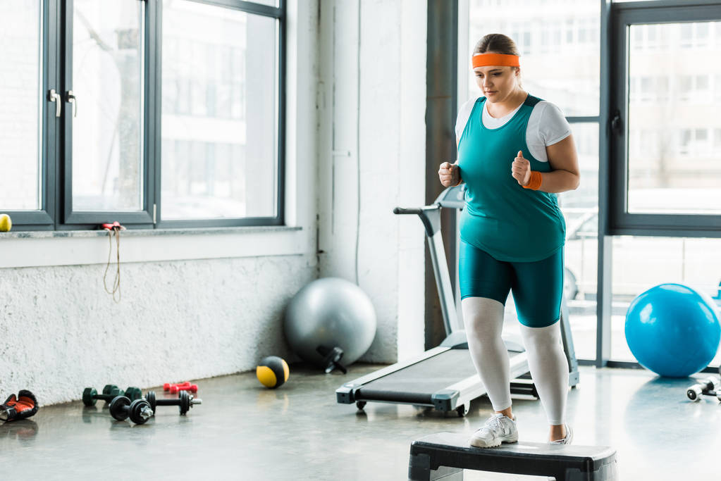 plus size woman exercising on step platform near sport equipment - Photo, Image