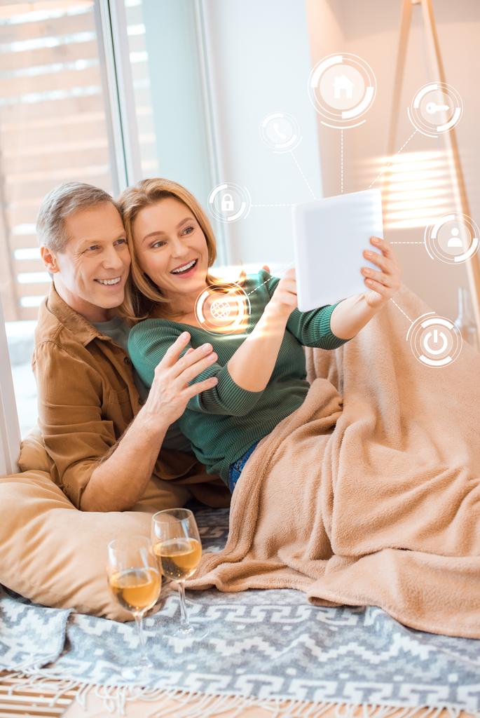 couple souriant à l'aide d'une tablette numérique tout en étant assis sous couverture polaire sur le sol, concept de maison intelligente
 - Photo, image