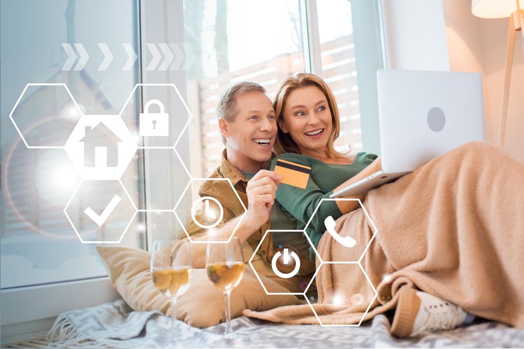happy wife pointing at laptop screen while smiling husband holding credit card, smart home concept - Photo, Image