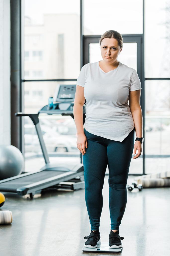 chateado mulher com sobrepeso em pé em escalas no ginásio
 - Foto, Imagem