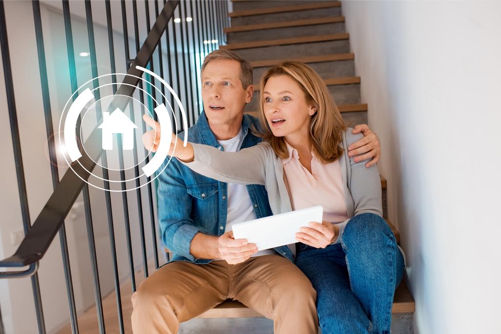 femme inspirée pointant la main tout en étant assis avec mari sur les escaliers et en utilisant une tablette numérique, concept de maison intelligente
 - Photo, image