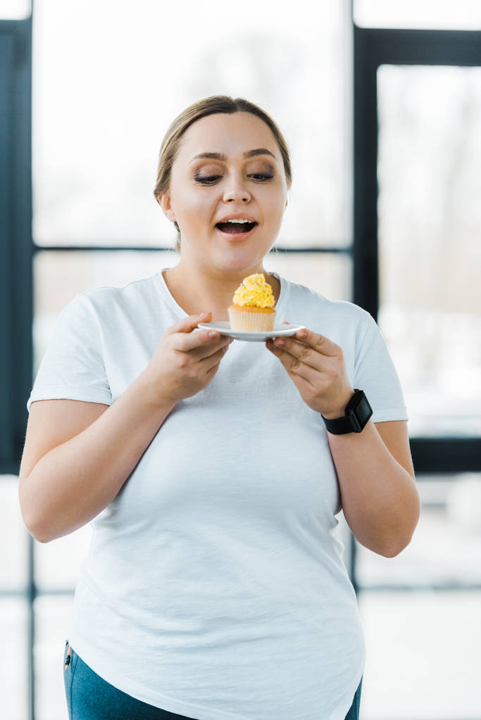 mulher sobrepeso feliz olhando para cupcake saboroso no ginásio
 - Foto, Imagem