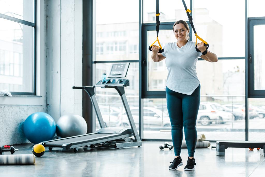brazos de entrenamiento de mujer con sobrepeso alegre con correas de suspensión en el gimnasio
 - Foto, Imagen
