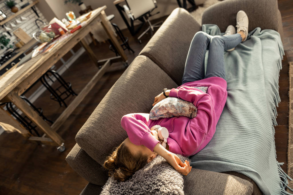 Adolescente menina abraçando pouco travesseiro e deitado no sofá em casa
 - Foto, Imagem