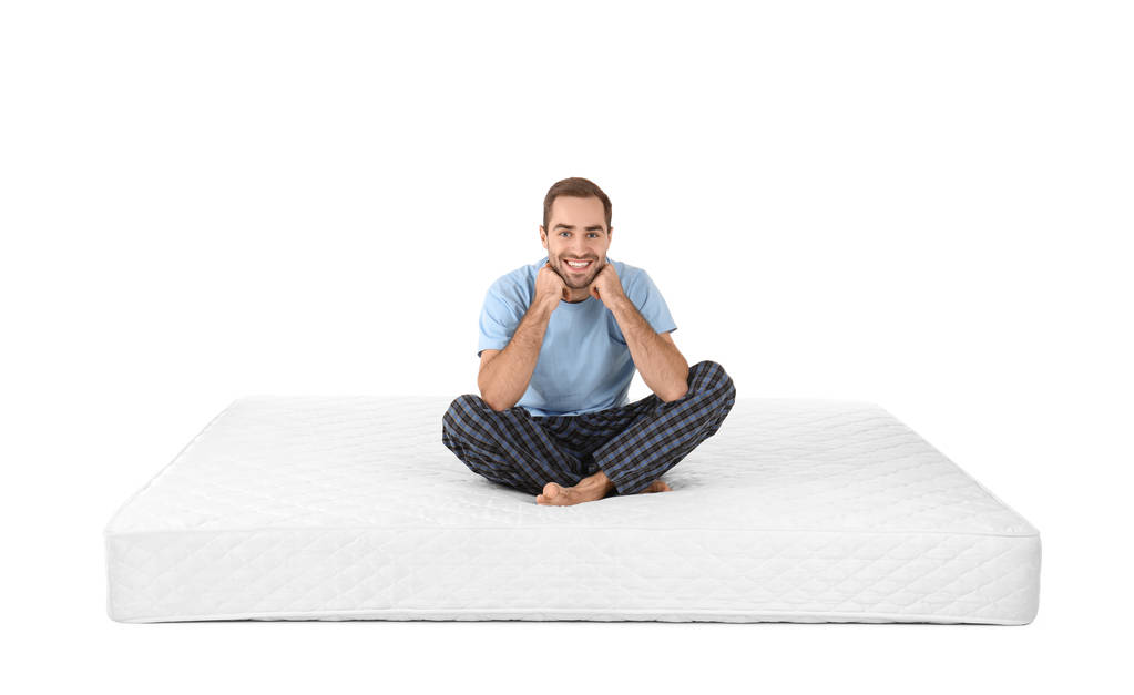 Young man sitting on mattress against white background - Photo, Image