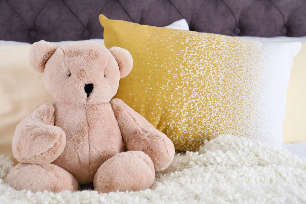 Милий плюшевий ведмідь сидить на ліжку в приміщенні. Простір для тексту
 - Фото, зображення