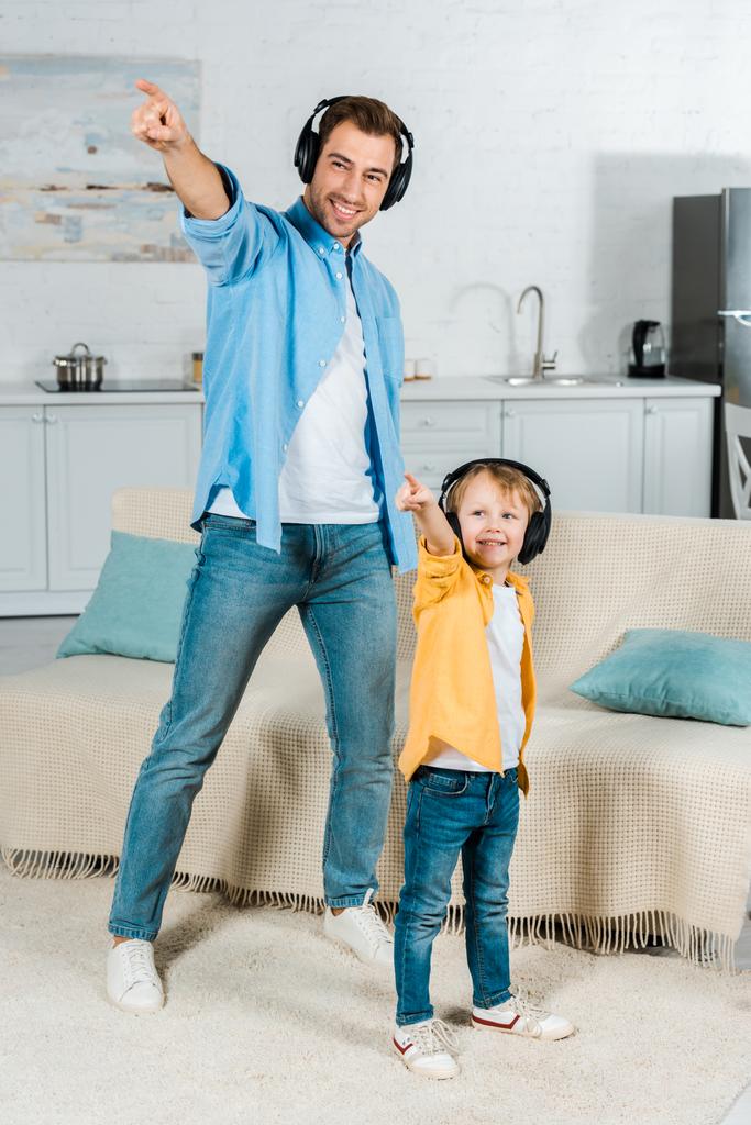 happy father with preschooler son in headphones listening music and pointing with fingers at home  - Photo, Image