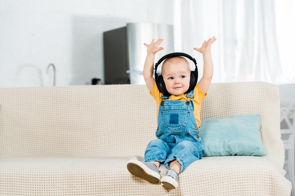 adorable male toddler in headphones with hands in air listening music at home with copy space - Photo, Image