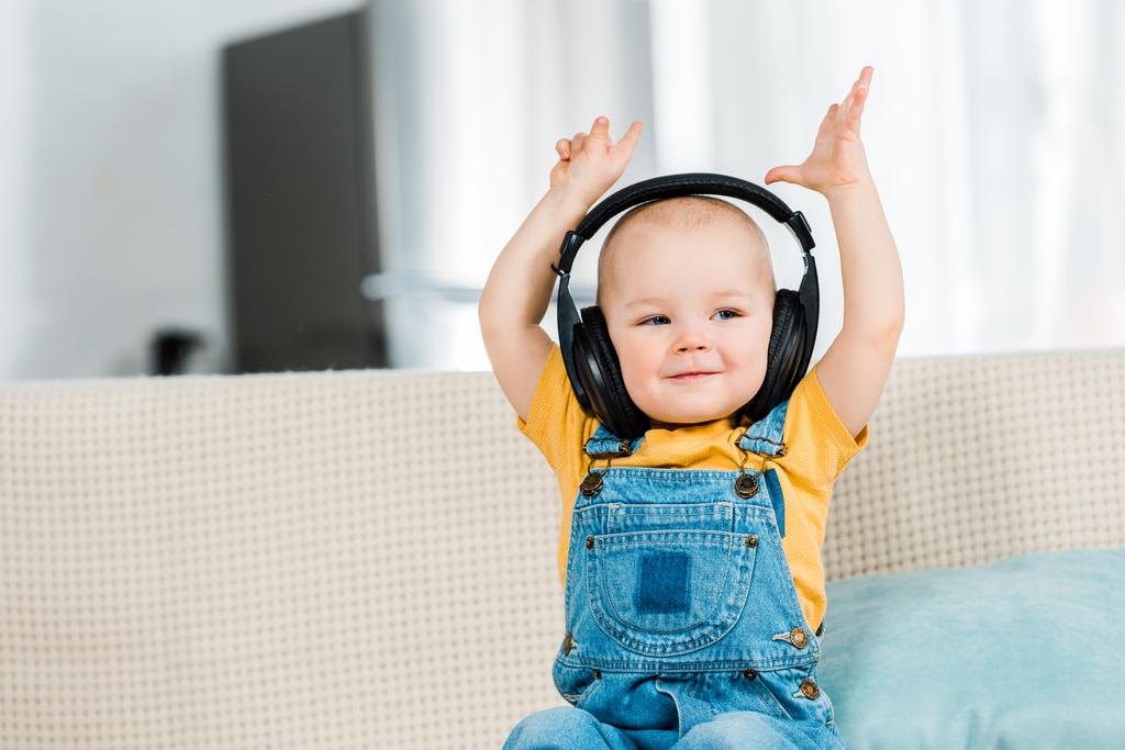 αξιολάτρευτο παιδί αρσενικό στα ακουστικά με τα χέρια στον αέρα που ακούει μουσική στο σπίτι - Φωτογραφία, εικόνα