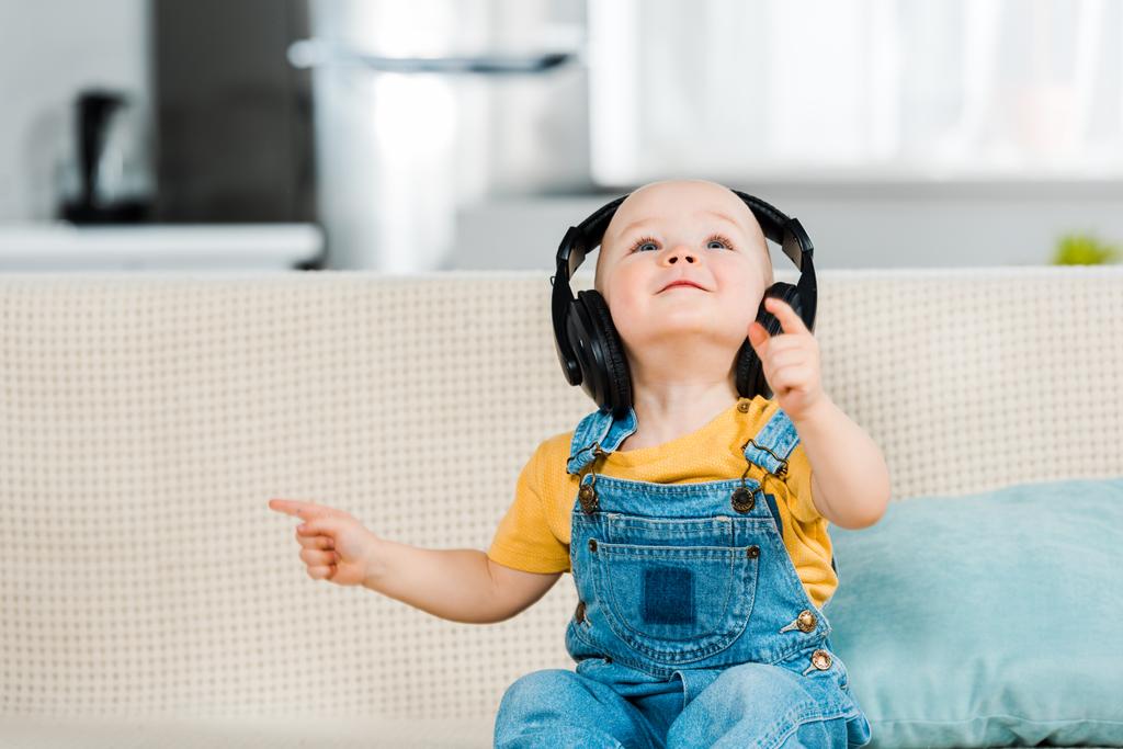 adorable male toddler in headphones sitting on couch and listening music at home - Photo, Image
