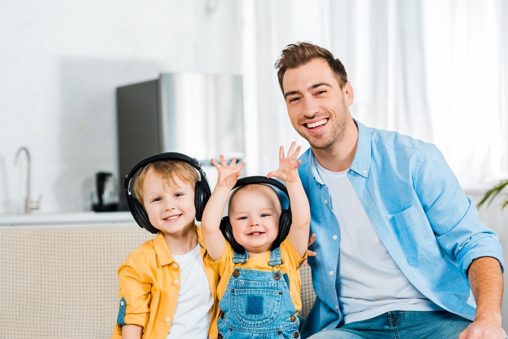usmívající se otec s roztomilé batole a preschooler syny ve sluchátkách doma při pohledu na fotoaparát  - Fotografie, Obrázek