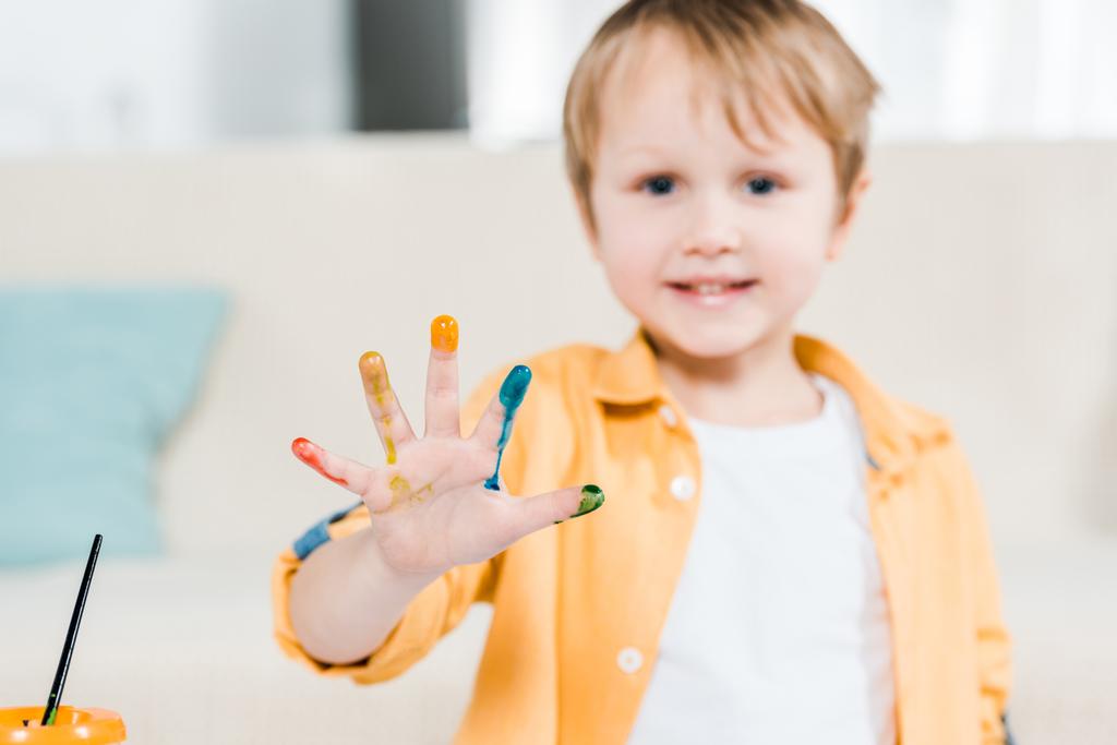 милый дошкольник с красочной краской на руке, глядя в камеру дома
 - Фото, изображение
