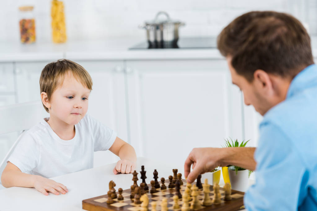 батько і дошкільник син сидить за столом і грає в шахи вдома
 - Фото, зображення
