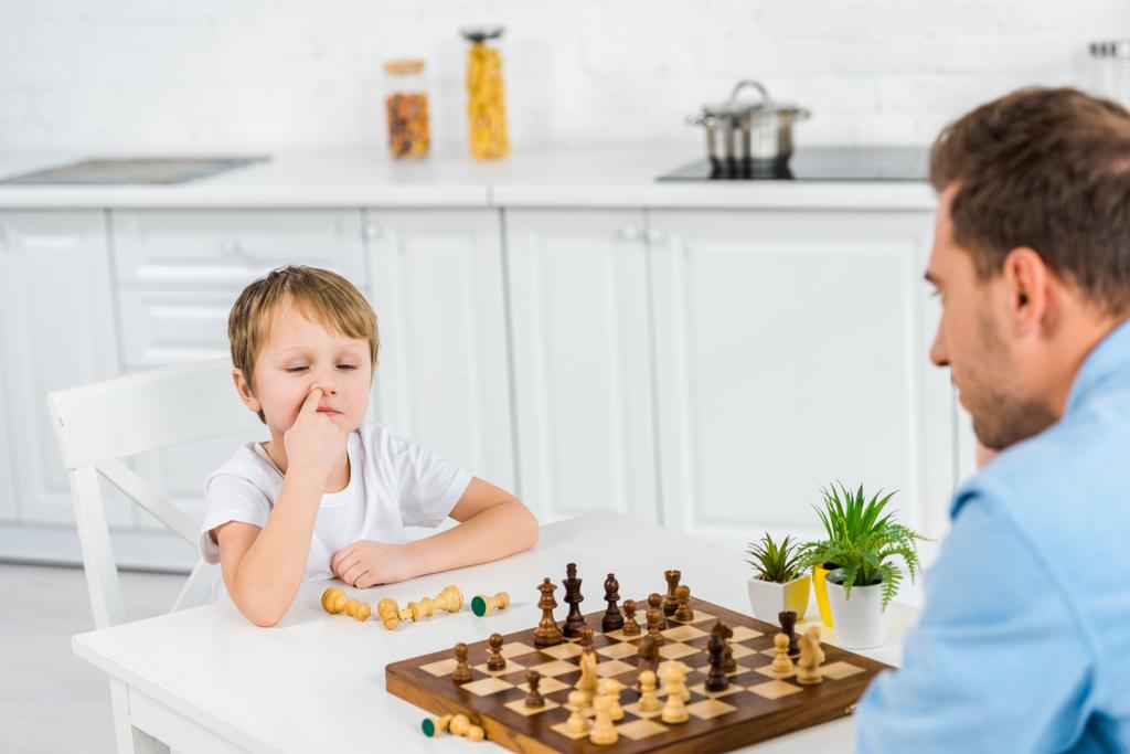 preescolar hijo escogiendo nariz mientras jugando ajedrez con padre en casa
 - Foto, Imagen