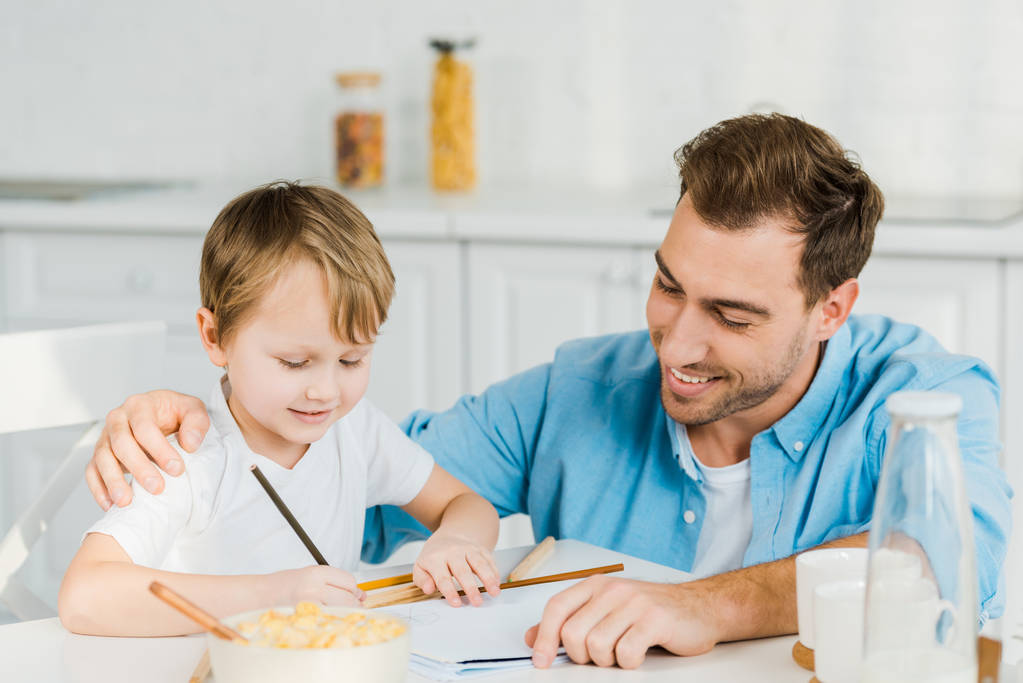 uśmiechający się Syn ojca i przedszkolak rysunek podczas śniadania w kuchni - Zdjęcie, obraz
