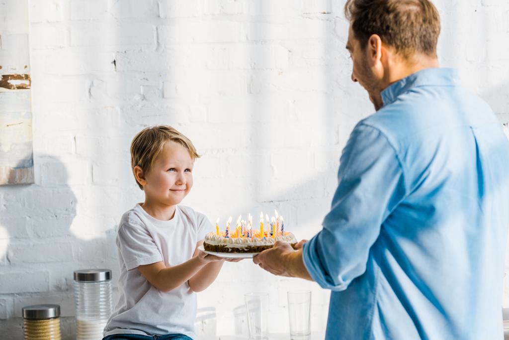 父は台所で愛らしい未就学児の息子に誕生日ケーキを与える - 写真・画像