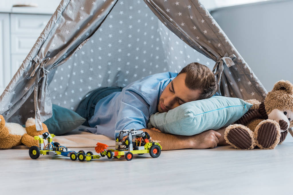 erwachsener Mann schläft auf Kissen in Wigwam mit Spielzeug herum  - Foto, Bild