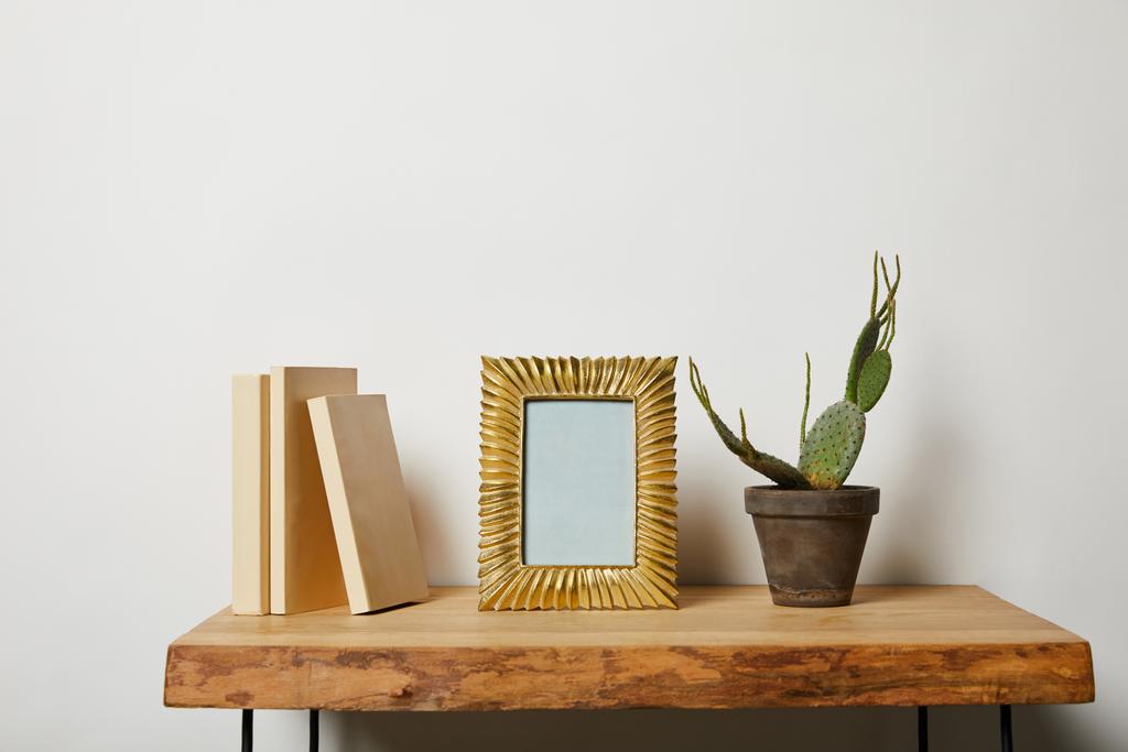 livres près de cadre doré et cactus en pot sur table en bois
  - Photo, image