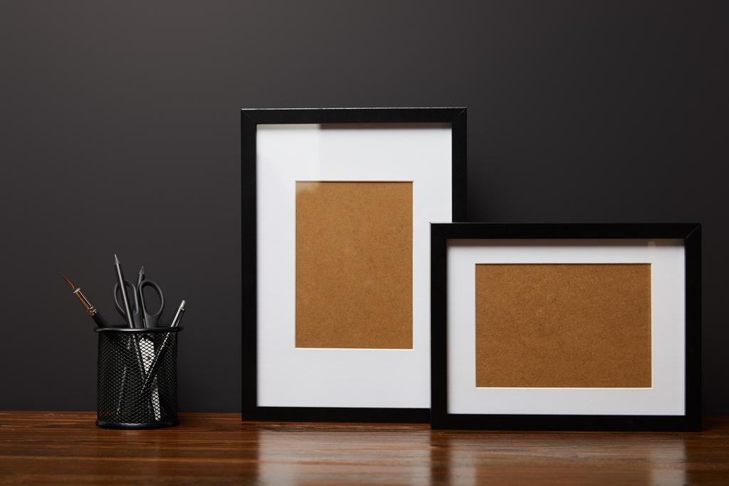 black square frames near metallic holder with stationery on wooden table  - Photo, Image