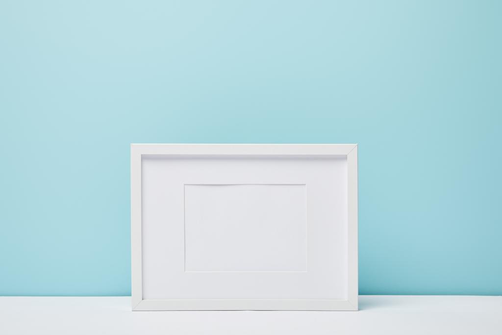 λευκό τετράγωνο πλαίσιο σε λευκή επιφάνεια κοντά μπλε τοίχο  - Φωτογραφία, εικόνα