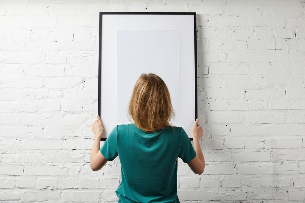 vista posterior de la mujer sosteniendo el póster de la maqueta en el marco
  - Foto, Imagen
