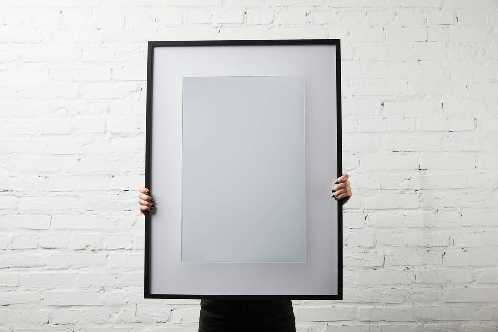 woman covering face while standing and holding blank black frame  - Photo, Image